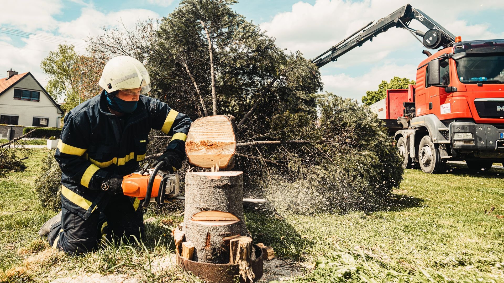 Firefighter using chainsaw to cut tree trunk with emergency truck nearby