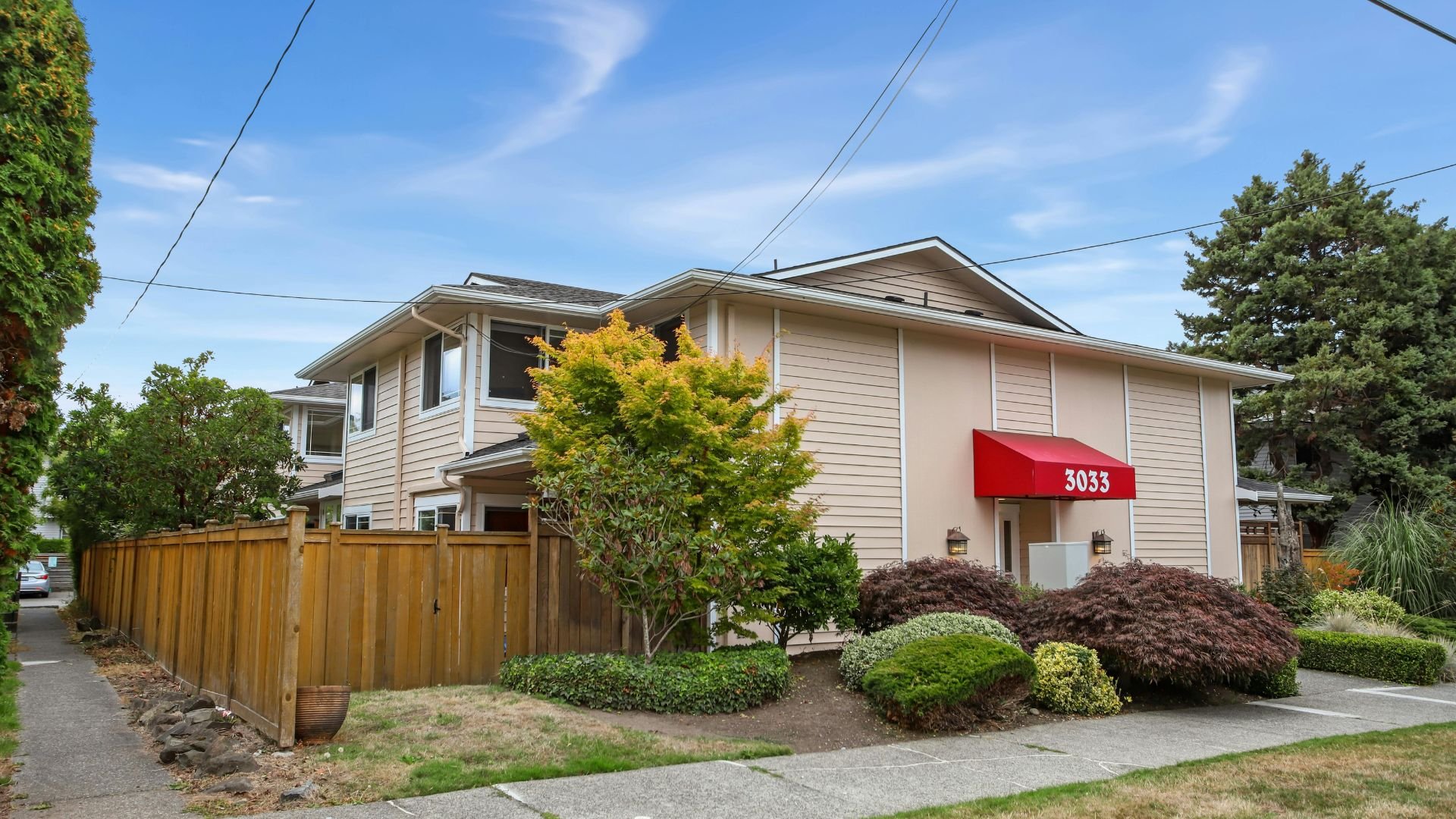 Two-story residential building with red awning, wooden fence, landscaped yard